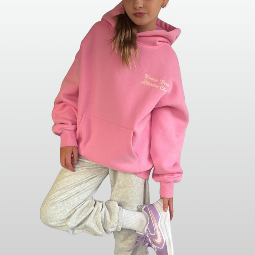 Child wearing a pink hoodie with text, light gray pants, and purple shoes on a white background