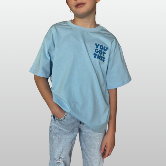 Child wearing a light blue t-shirt with 'YOU GOT THIS' text on a plain background